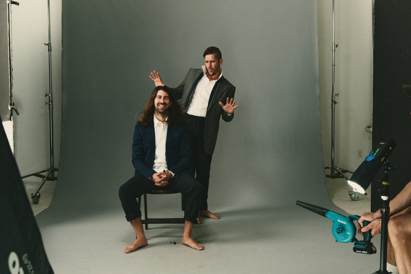 Seated on a chair in suits while a leaf blower is aimed at them