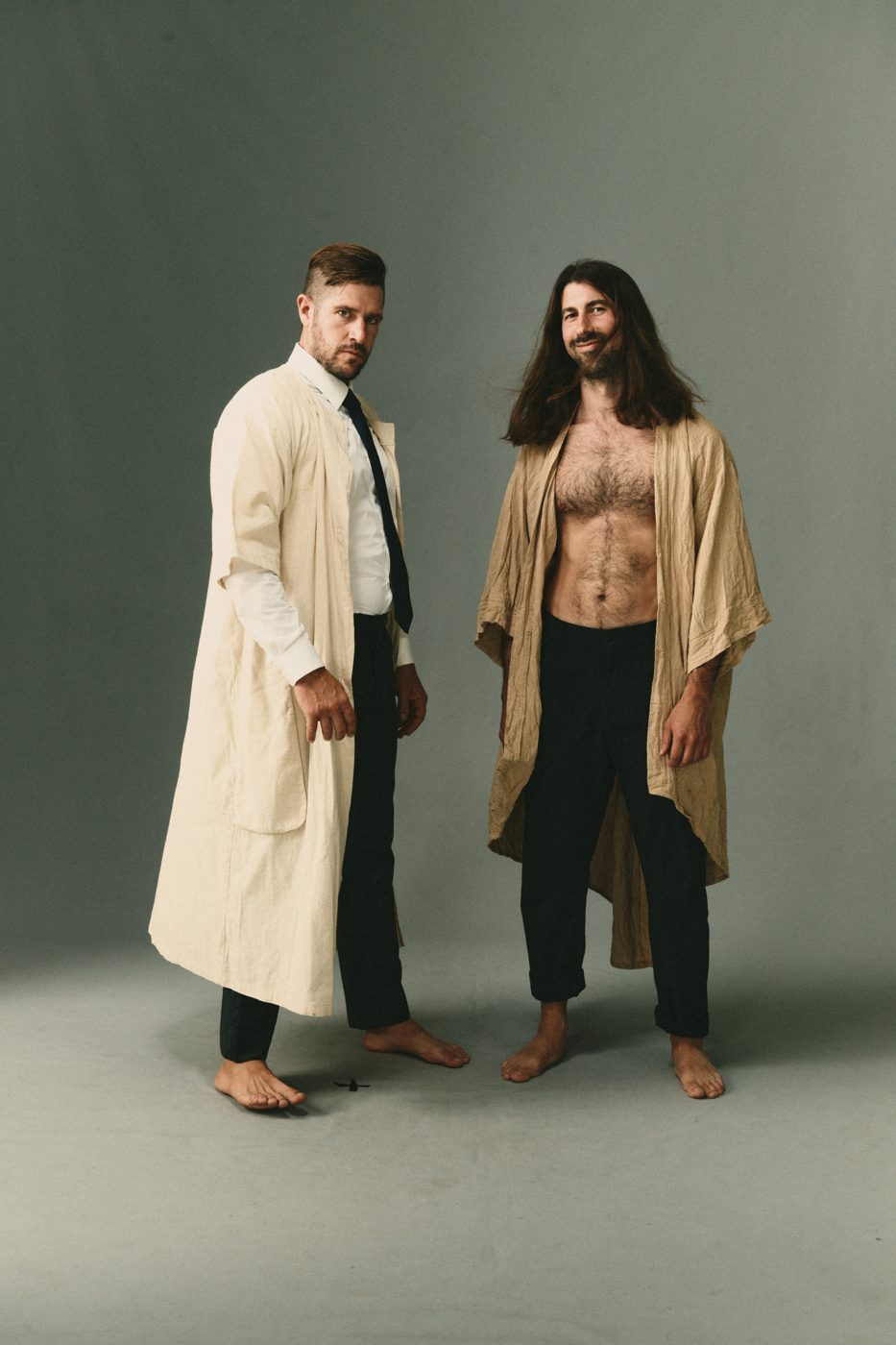 Two men in robes, one shirt open, staring down the lens