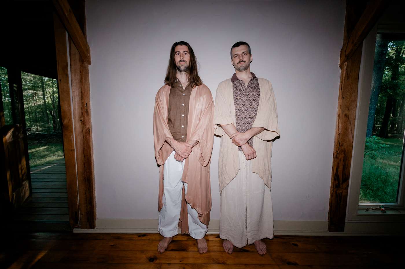 Two men in robes standing in a timber-frame doorway, lit by flash, forest behind.