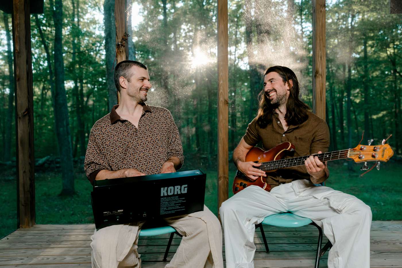 On the porch, turned toward each other, one with a bass and one behind a synthesizer.