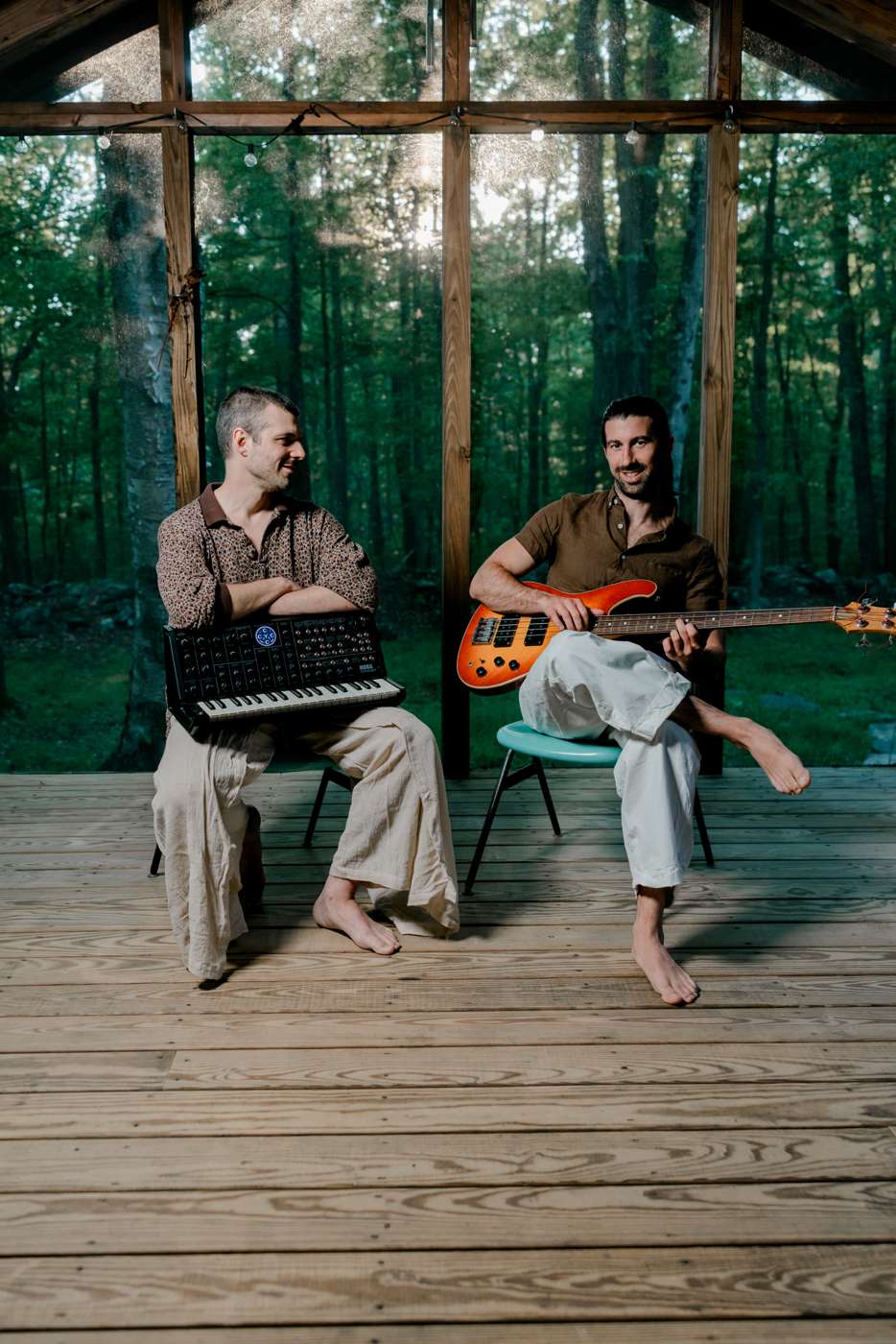 Vertical: seated on the porch in the woods, a Korg synthesizer across the lap, bass in the background.